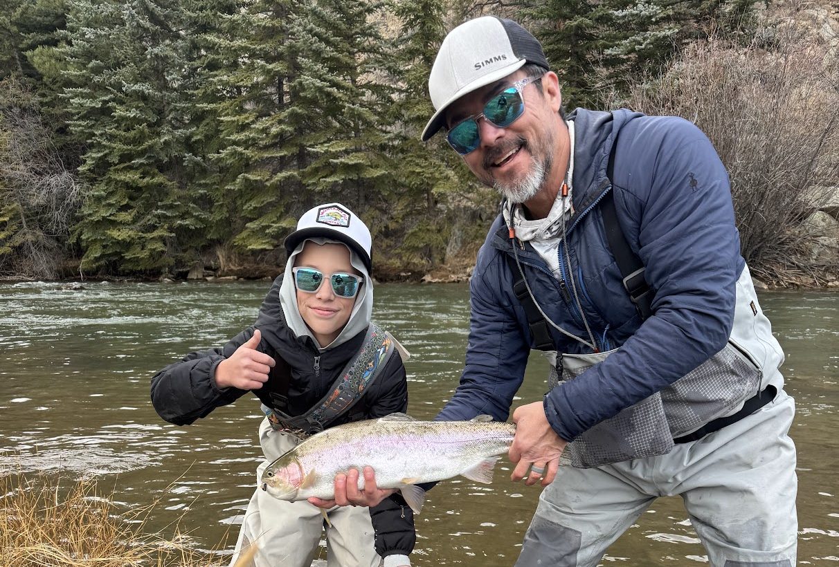 Youth angler holding a trout with an instructor